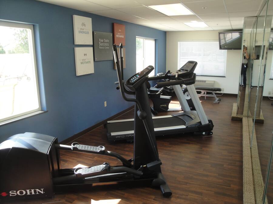 A fitness center with treadmills and elliptical machines, motivational posters on the wall, and a large mirror.