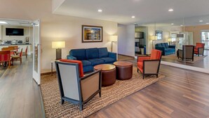 Una sala de estar moderna con un sofá azul, sillones rojos y una mesa de centro. Hay un televisor montado en la pared y un comedor al fondo.