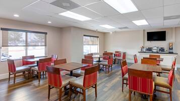 A dining area with wooden tables and chairs, large windows, and a kitchen area with appliances.