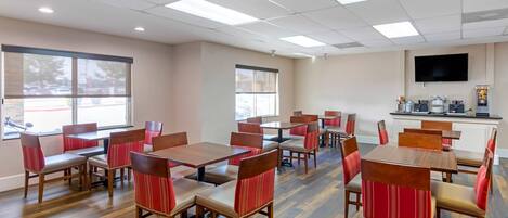 A dining area with wooden tables and chairs, large windows, and a kitchen area with appliances.