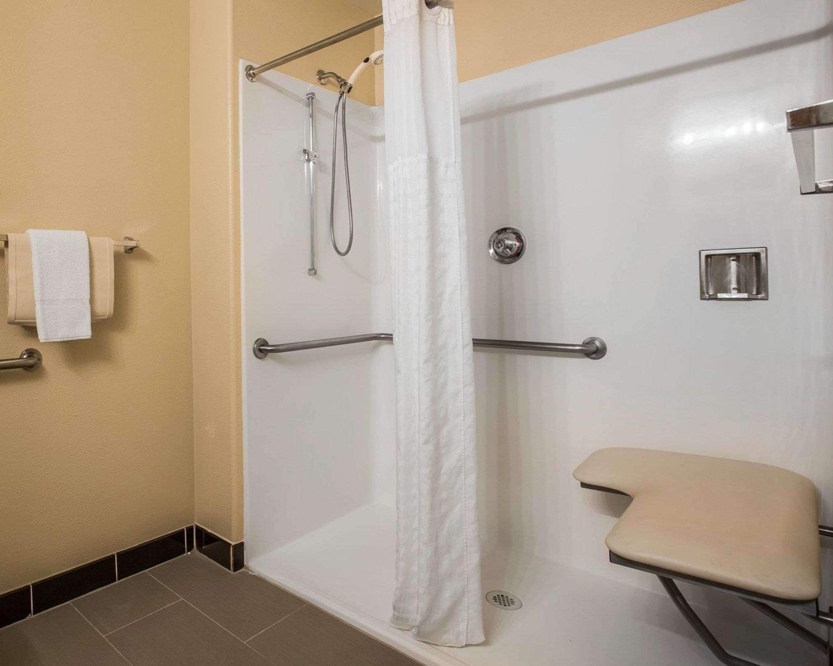 A wheelchair-accessible shower stall with a white curtain, grab bars, and a handheld showerhead.