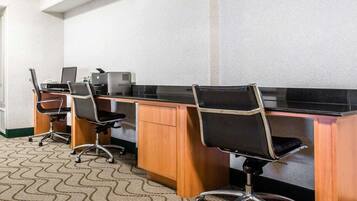 Uma sala de conferências com três mesas, cada uma com um computador e uma impressora. O chão é coberto por carpete e as mesas são de madeira.