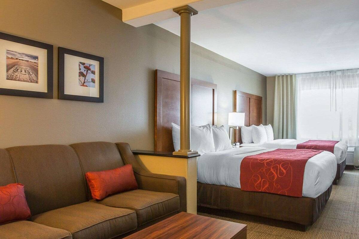 A hotel room with a sofa, two beds, a wooden coffee table, and framed pictures on the wall.