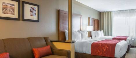 Habitación de hotel con sofá, dos camas, una mesita de madera y cuadros enmarcados en la pared.