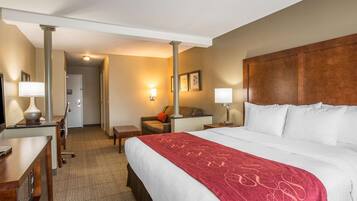 A hotel room with a large bed, a desk, a chair, a sofa, and a bedside table.