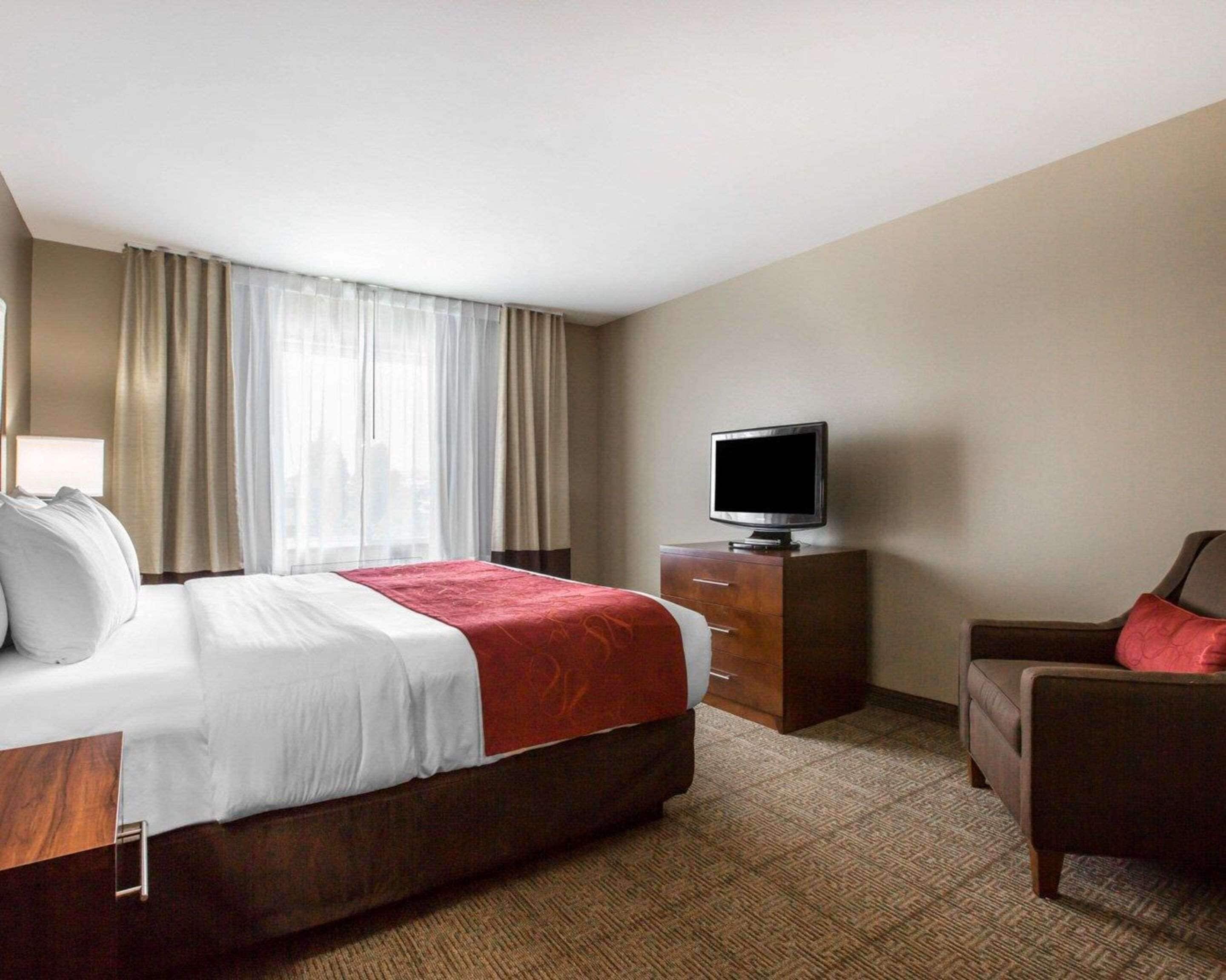 A hotel room with a bed, a TV on a wooden cabinet, a chair, and a window with curtains.