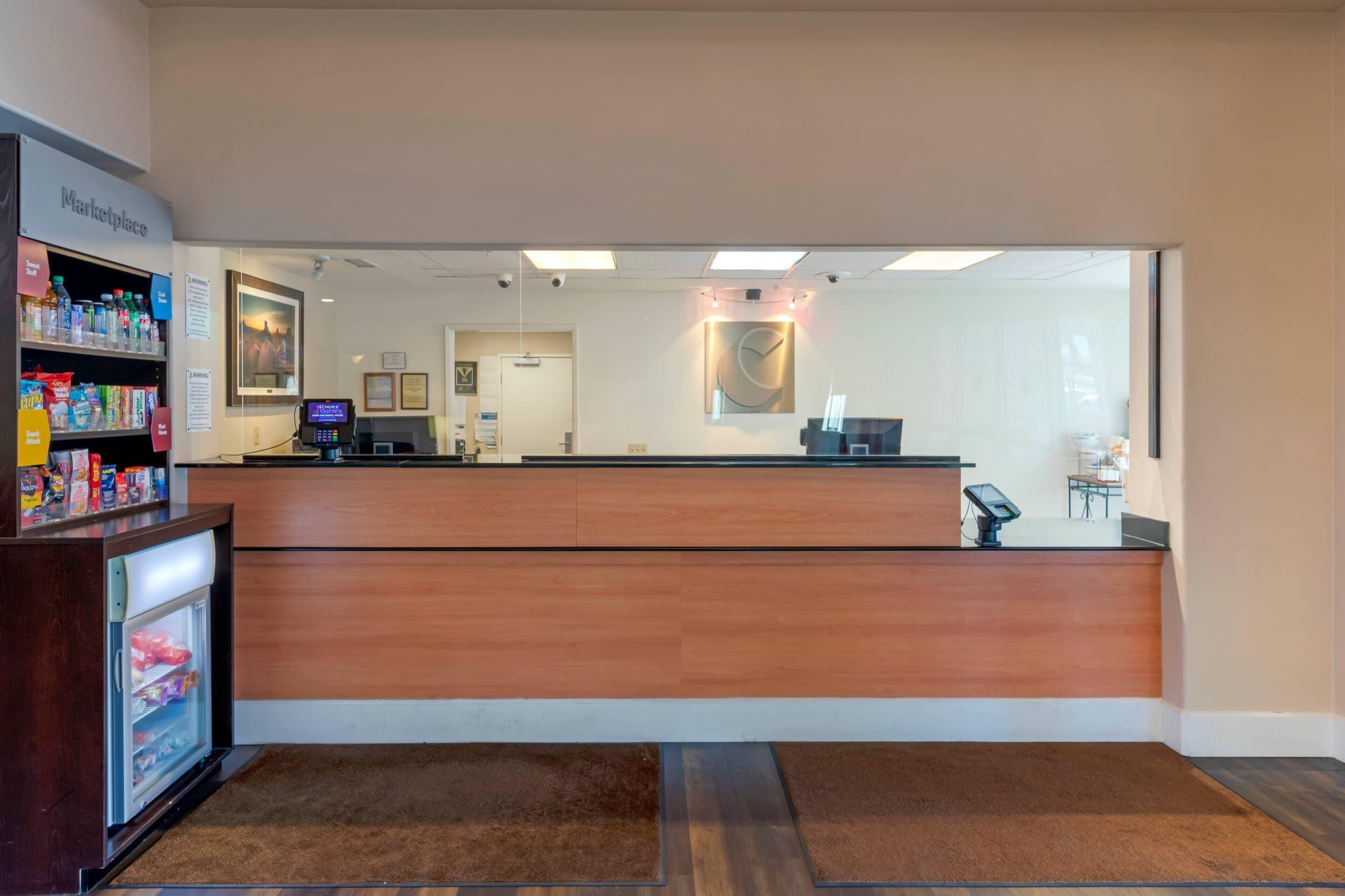 Una zona de recepción con mostrador de madera, vitrina refrigerada y un pequeño quiosco con pantalla digital.