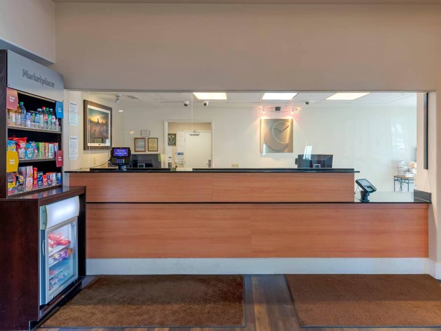 Una zona de recepción con mostrador de madera, vitrina refrigerada y un pequeño quiosco con pantalla digital.