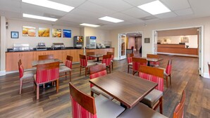 Un comedor moderno con mesas y sillas de madera, una encimera de cocina con electrodomésticos y un mostrador de recepción.