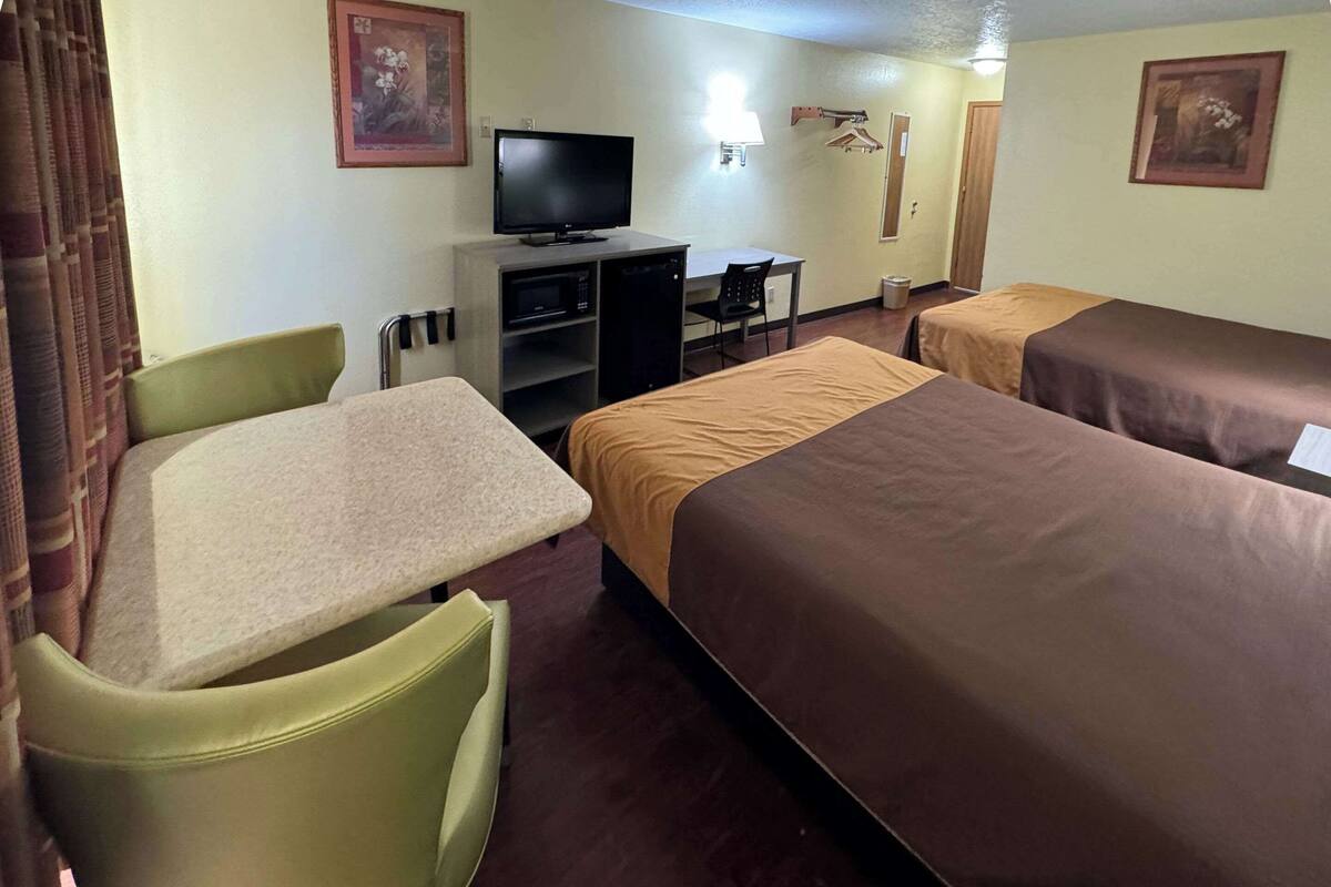 Quarto de hotel com duas camas, uma escrivaninha, uma televisão e uma cadeira.