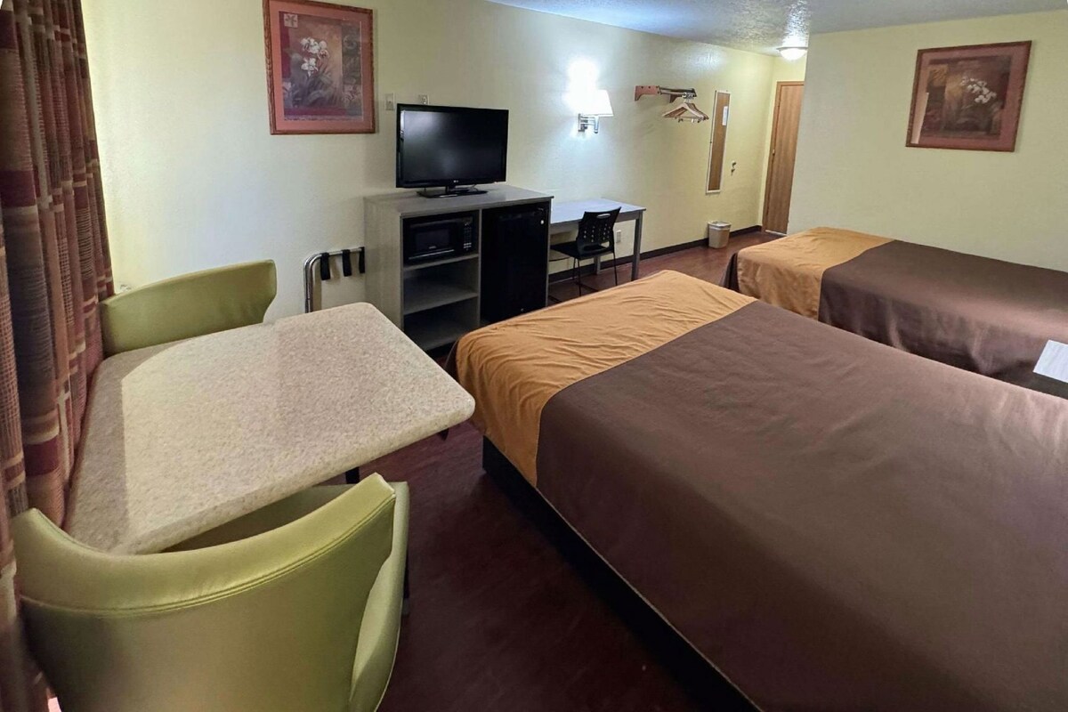 A hotel room with a single bed, a desk with a chair, a television, and a small seating area.