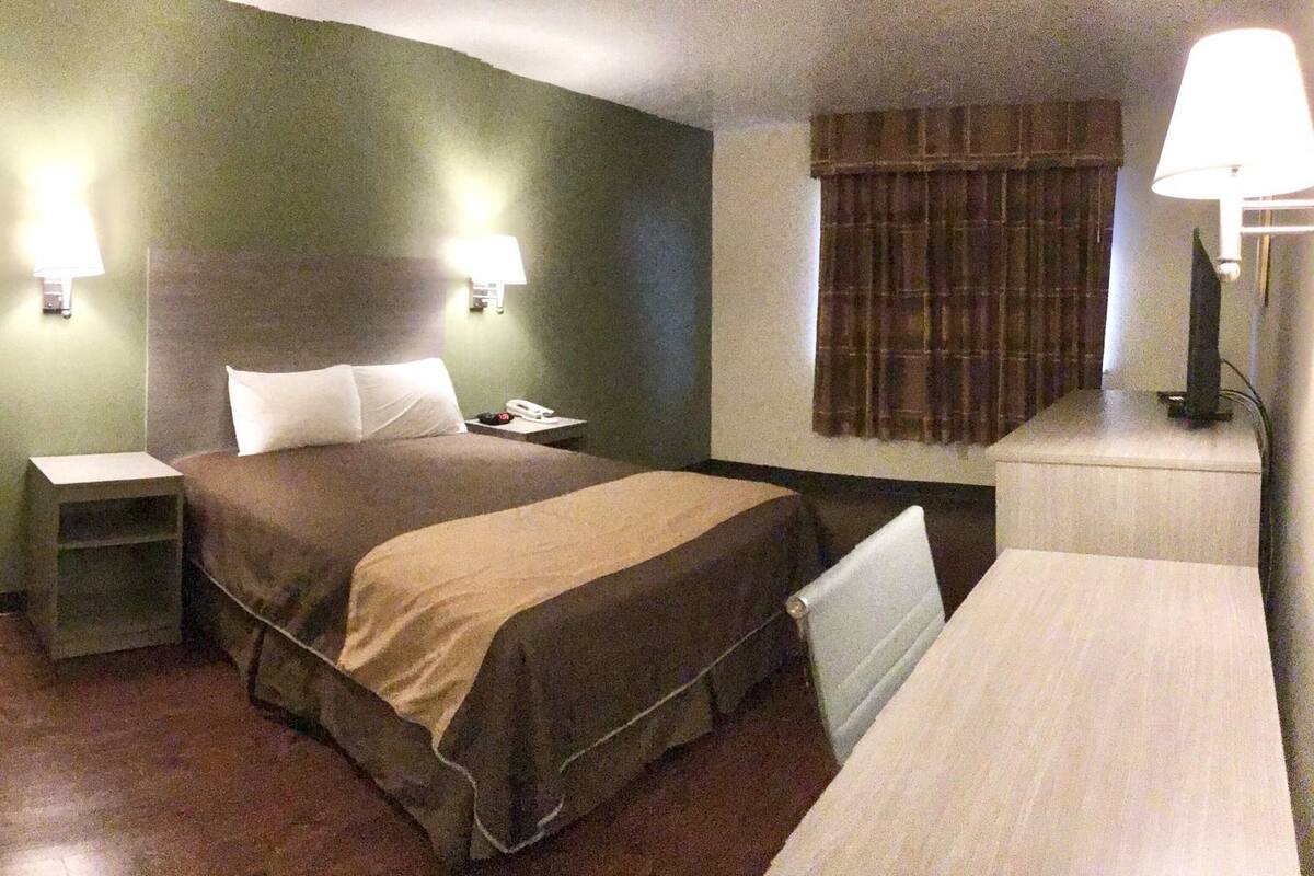 Quarto de hotel com cama, mesas de cabeceira, escrivaninha e luminária.