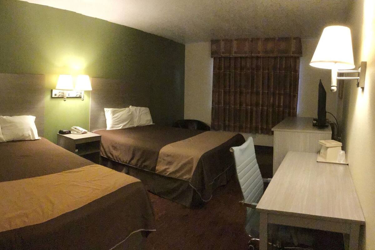 Quarto de hotel com duas camas, uma mesa, uma cadeira, um telefone e um abajur.