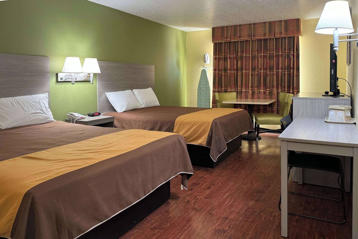 Quarto de hotel com duas camas, uma escrivaninha, uma cadeira e uma mesa.