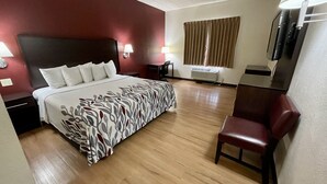 A hotel room with a bed, a desk, a chair, a TV, and an air conditioning unit. - Red Roof Inn Sandusky - Milan (Milan)