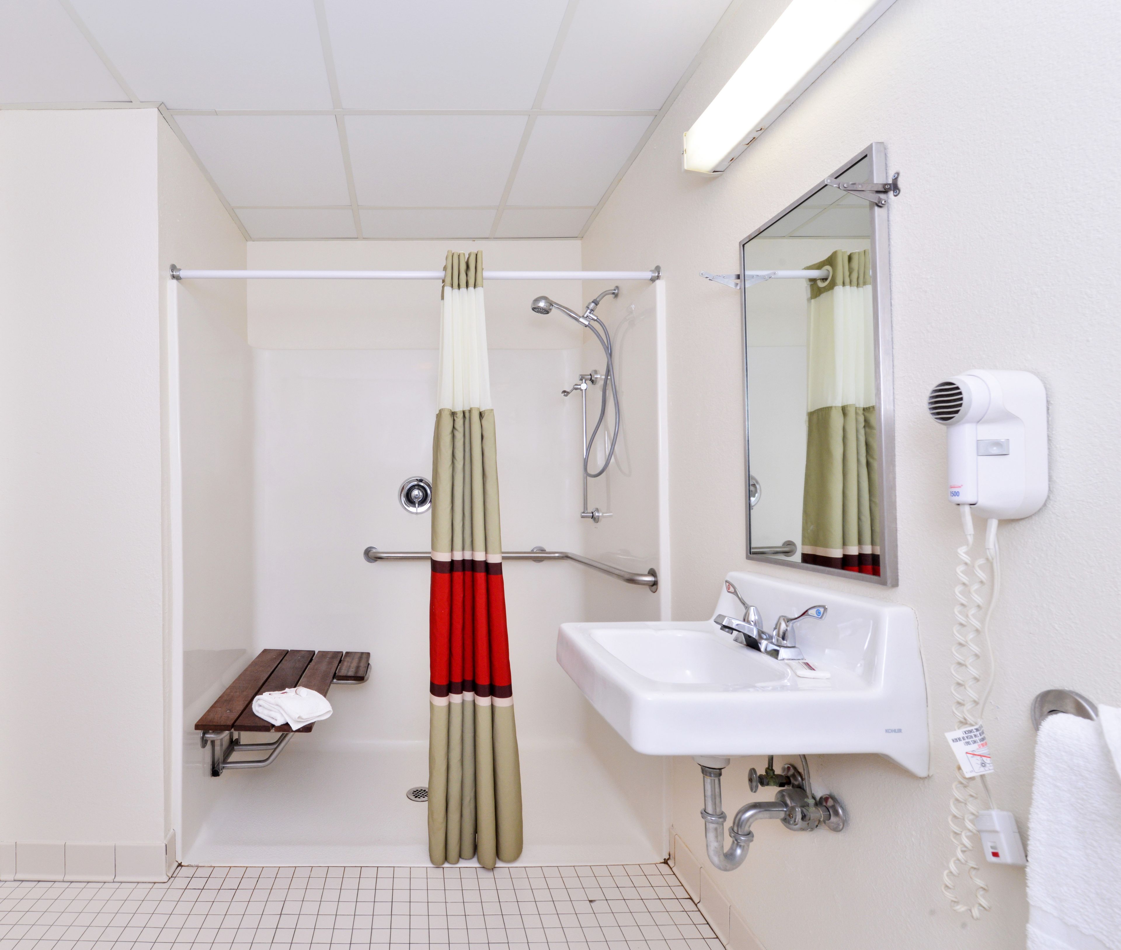 A bathroom with a shower, a sink, a mirror, a towel rack, and a hairdryer.