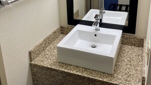 A bathroom with a white sink, granite countertop, and a mirror with a black frame. - Red Roof Inn Sandusky - Milan (Milan)