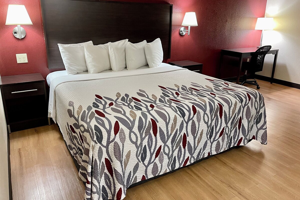 A neatly made bed with a patterned bedspread, two bedside lamps, a nightstand, and a desk with a chair.