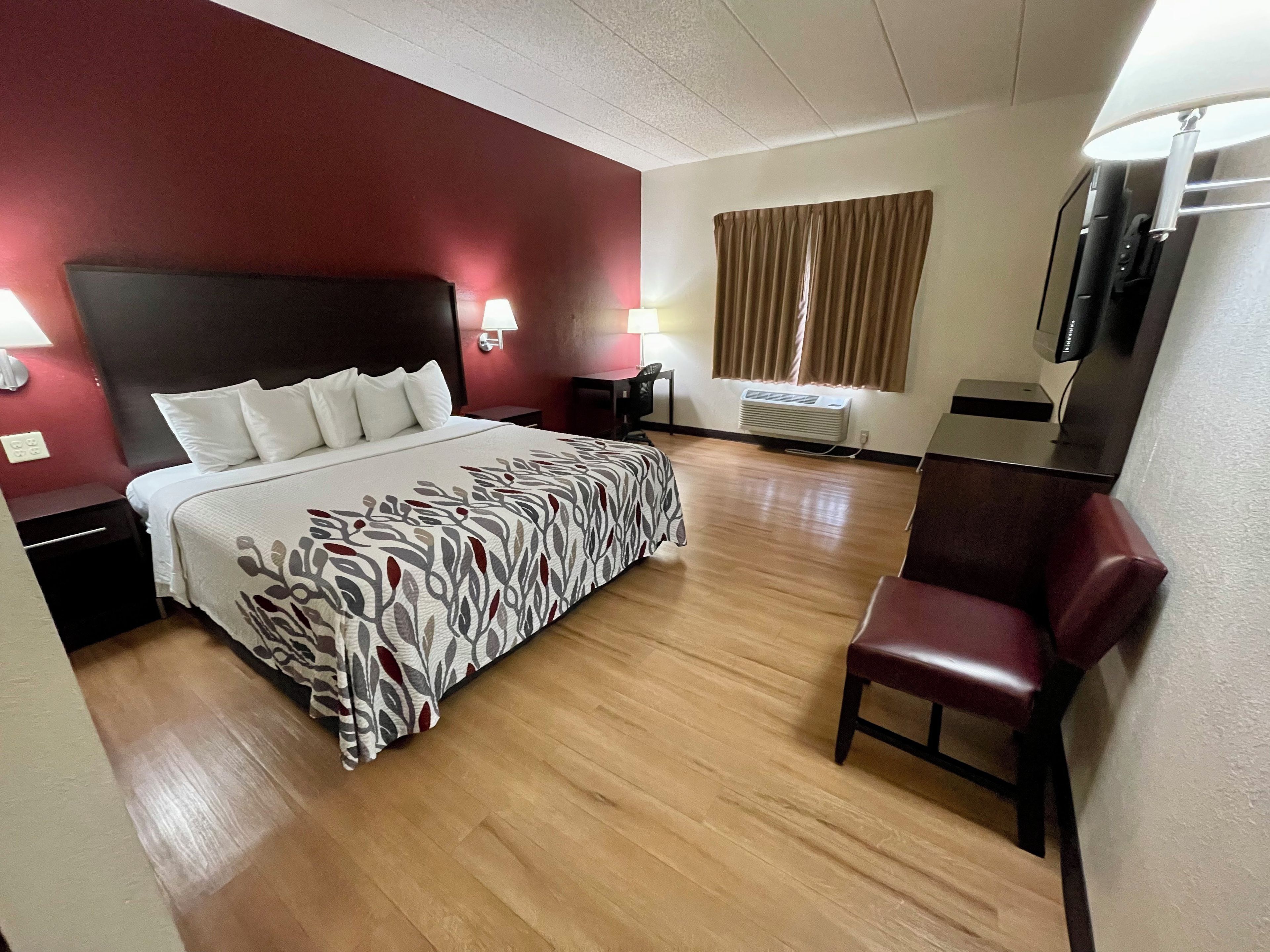 Habitación de hotel con cama, mesitas de noche, escritorio, silla, televisión y ventana con cortinas.