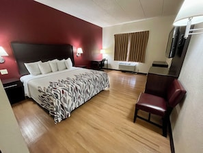 Quarto de hotel com cama, mesas de cabeceira, escrivaninha, cadeira, televisão e janela com cortinas.