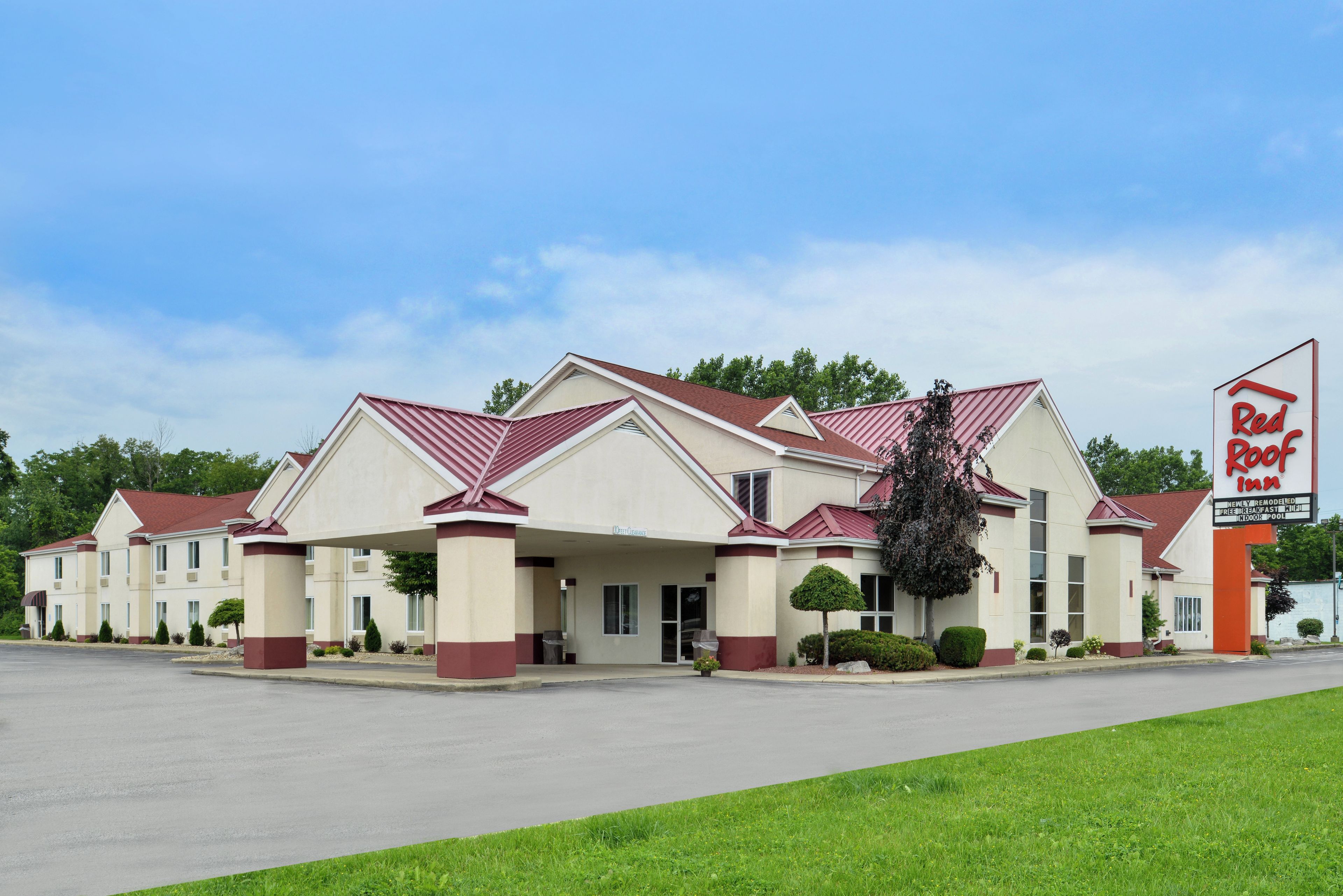 A Red Roof Inn with a two-story building, a covered parking area, and a sign indicating amenities like a newly remodeled interior, free breakfast, and an indoor pool.