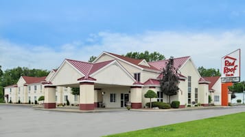 A Red Roof Inn with a two-story building, a covered parking area, and a sign indicating amenities like a newly remodeled interior, free breakfast, and an indoor pool.