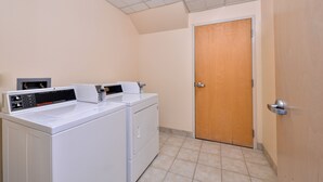 A laundry room with two white front-loading washers and dryers, a control panel, and a wooden door. - Red Roof Inn Sandusky - Milan (Milan)