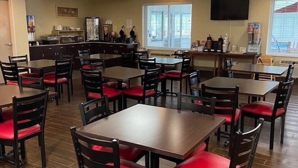 A restaurant with multiple tables and chairs, a counter with a beverage dispenser, and a television mounted on the wall. - Red Roof Inn Sandusky - Milan (Milan)