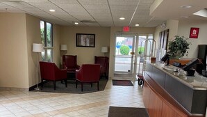 A hotel lobby with a reception desk, red seating area, and a view of the outside through a glass door. - Red Roof Inn Sandusky - Milan (Milan)