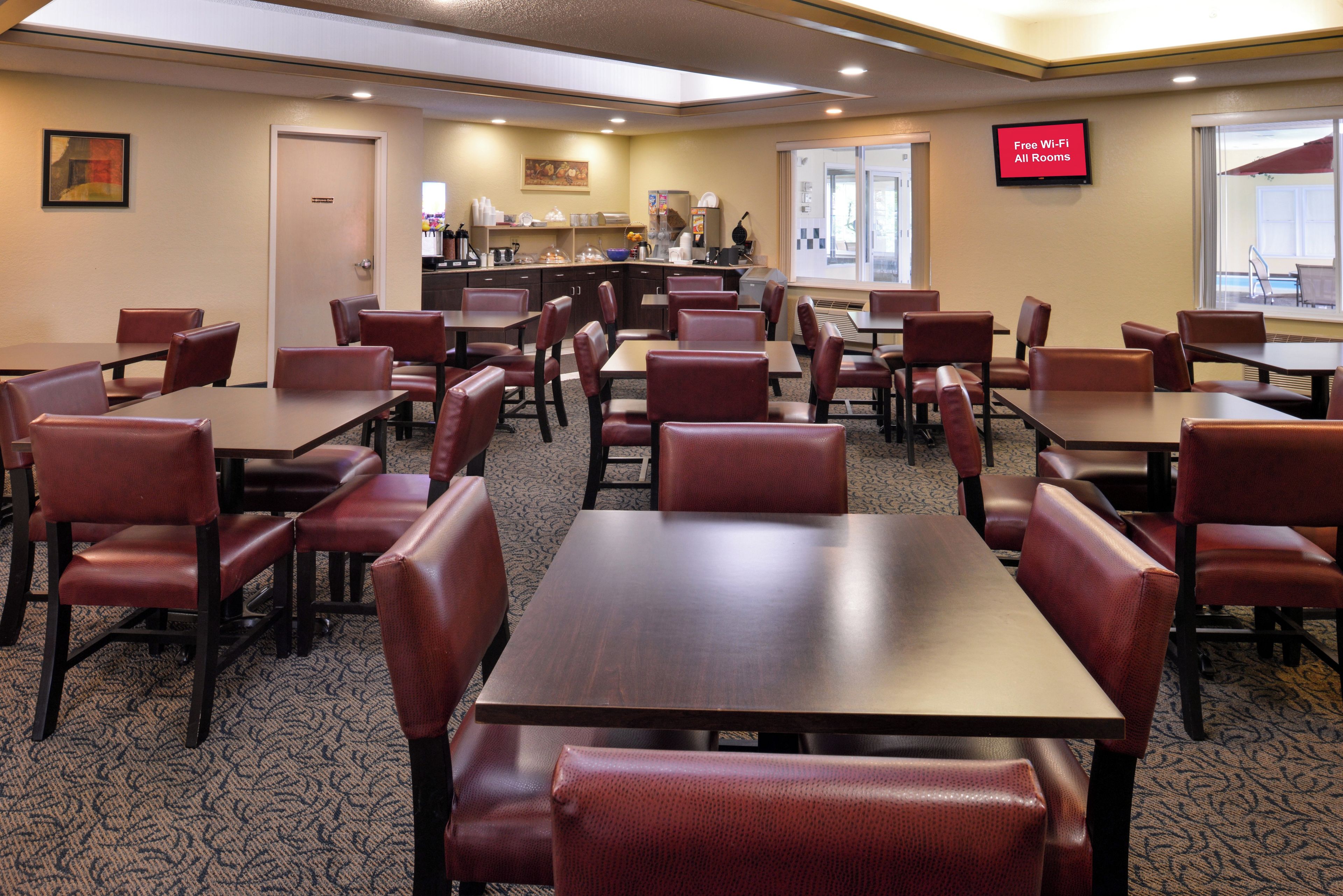 A hotel room with multiple tables and chairs, a kitchenette, a coffee station, and a sign indicating free Wi-Fi availability.