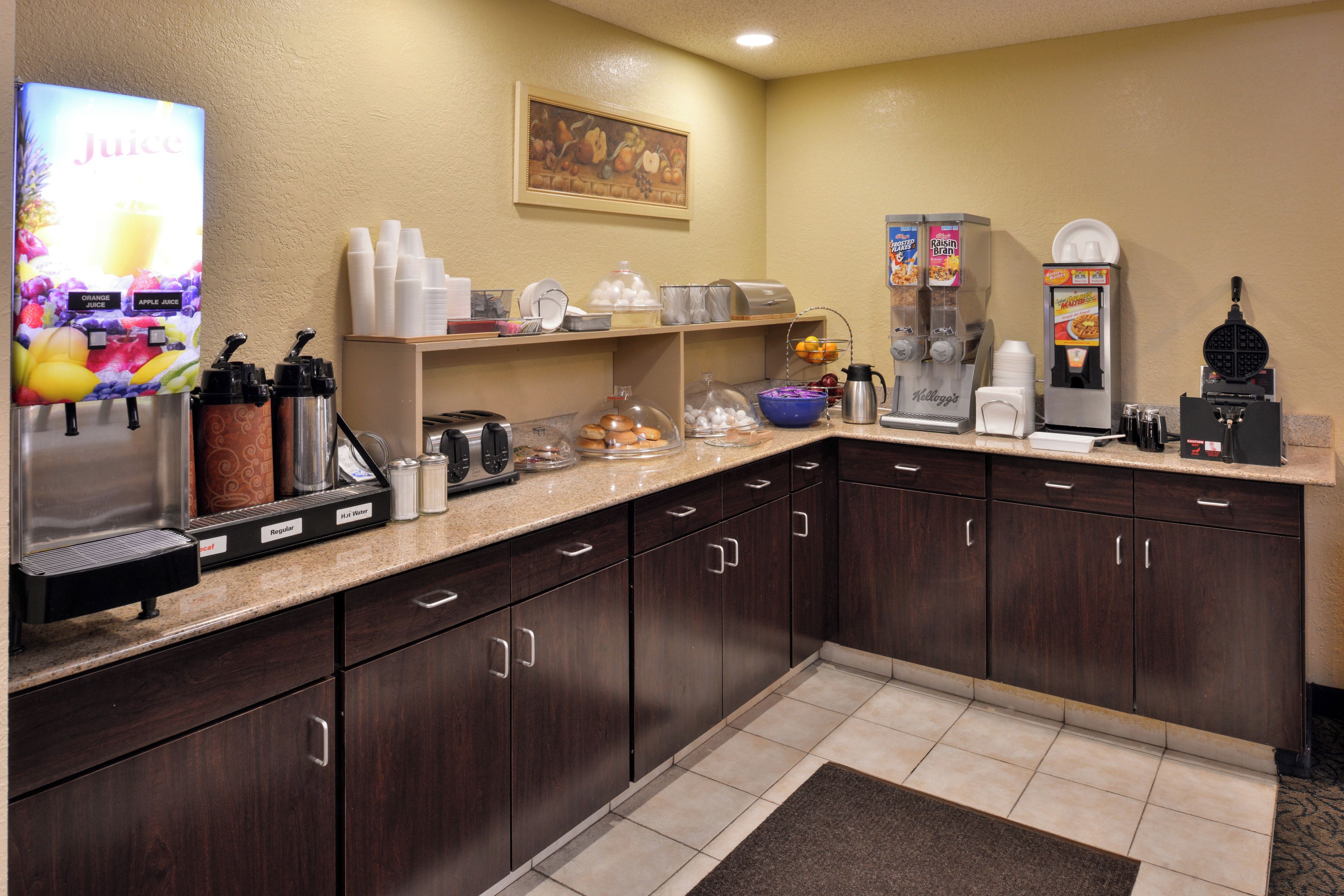 A hotel kitchen with juice dispensers, a waffle maker, and a coffee machine.