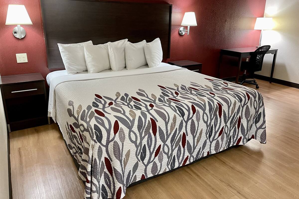 A neatly made bed with a patterned bedspread, two bedside lamps, a nightstand, and a desk with a chair.