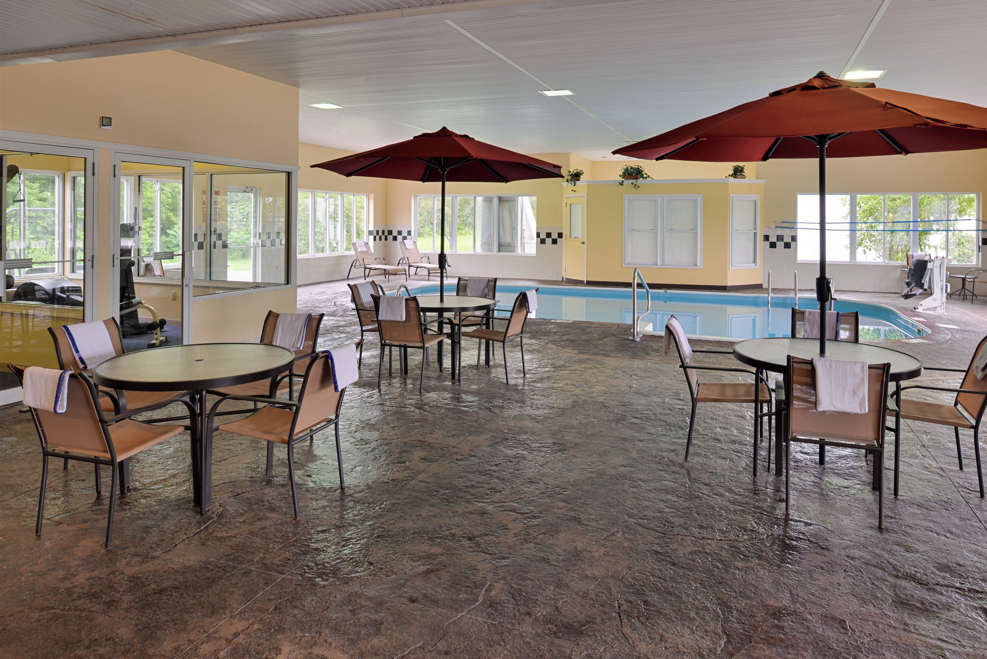 Un área de piscina interior con varias mesas y sillas, grandes sombrillas y una vista despejada de la piscina.