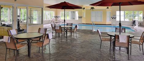 Un espace piscine intérieur doté de nombreuses tables et chaises, de grands parasols et offrant une vue dégagée sur la piscine.