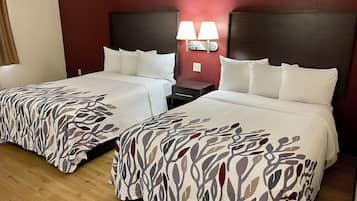 Habitación de hotel con dos camas, cada una con ropa blanca y cubrecama estampado con hojas. Hay dos mesitas de noche con lámparas, y las paredes están pintadas de rojo.