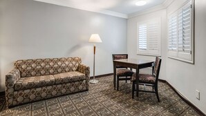 A room with a patterned sofa, a dining table with chairs, a floor lamp, and patterned flooring. - Rodeway Inn Old Town Temecula (Temecula)
