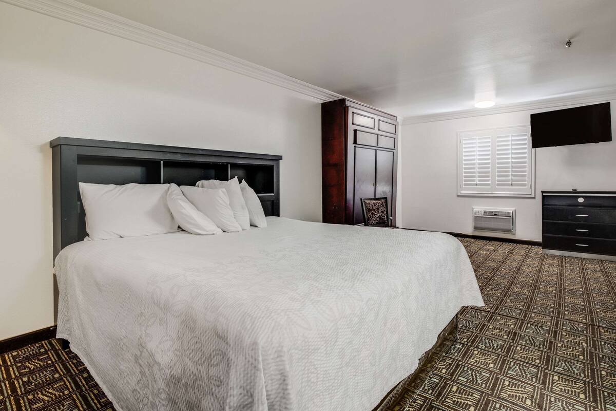 A hotel room with a large bed, a wardrobe, a television, and a window with blinds.