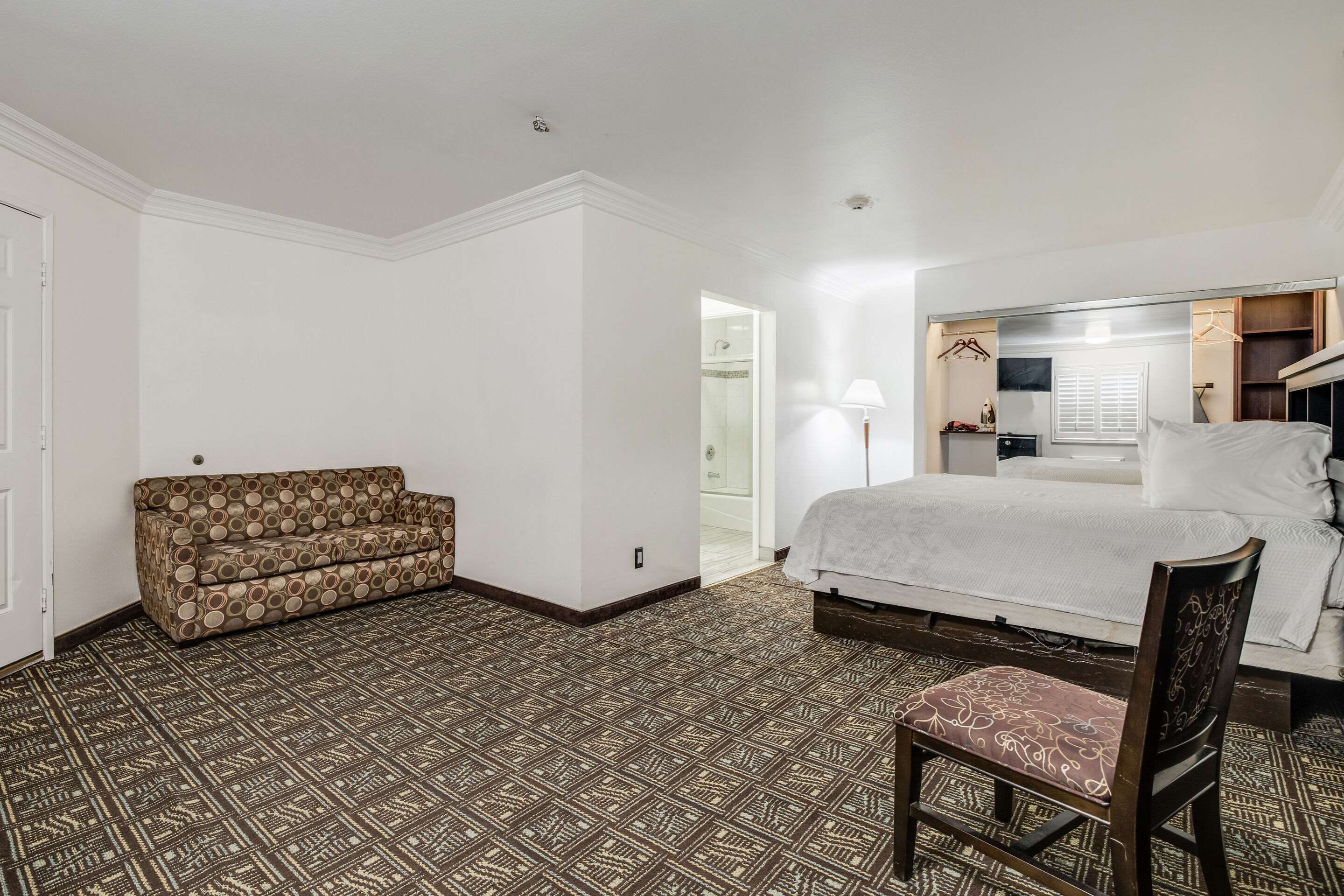 A hotel room with a patterned floor, a sofa, a bed, a chair, and a wardrobe.