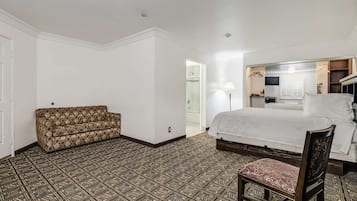 A hotel room with a patterned floor, a sofa, a bed, a chair, and a wardrobe.
