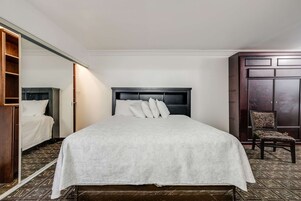 A neatly made bed with a white bedspread and pillows, a dark headboard, a wooden wardrobe, and a patterned carpet.