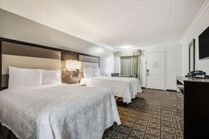 A hotel room with two beds, a desk, a chair, a lamp, and a patterned carpet.
