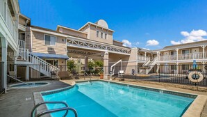 A swimming pool with a clear blue water, surrounded by a building with a covered walkway and outdoor seating. - Rodeway Inn Old Town Temecula (Temecula)