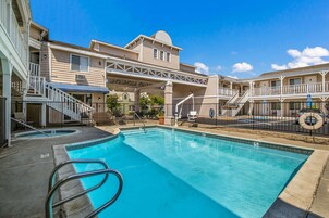 A swimming pool with a clear blue water, surrounded by a building with a covered walkway and outdoor seating.