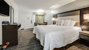 A hotel room with a large bed, a desk with a telephone, a television, and a patterned carpet. - Rodeway Inn Old Town Temecula (Temecula)