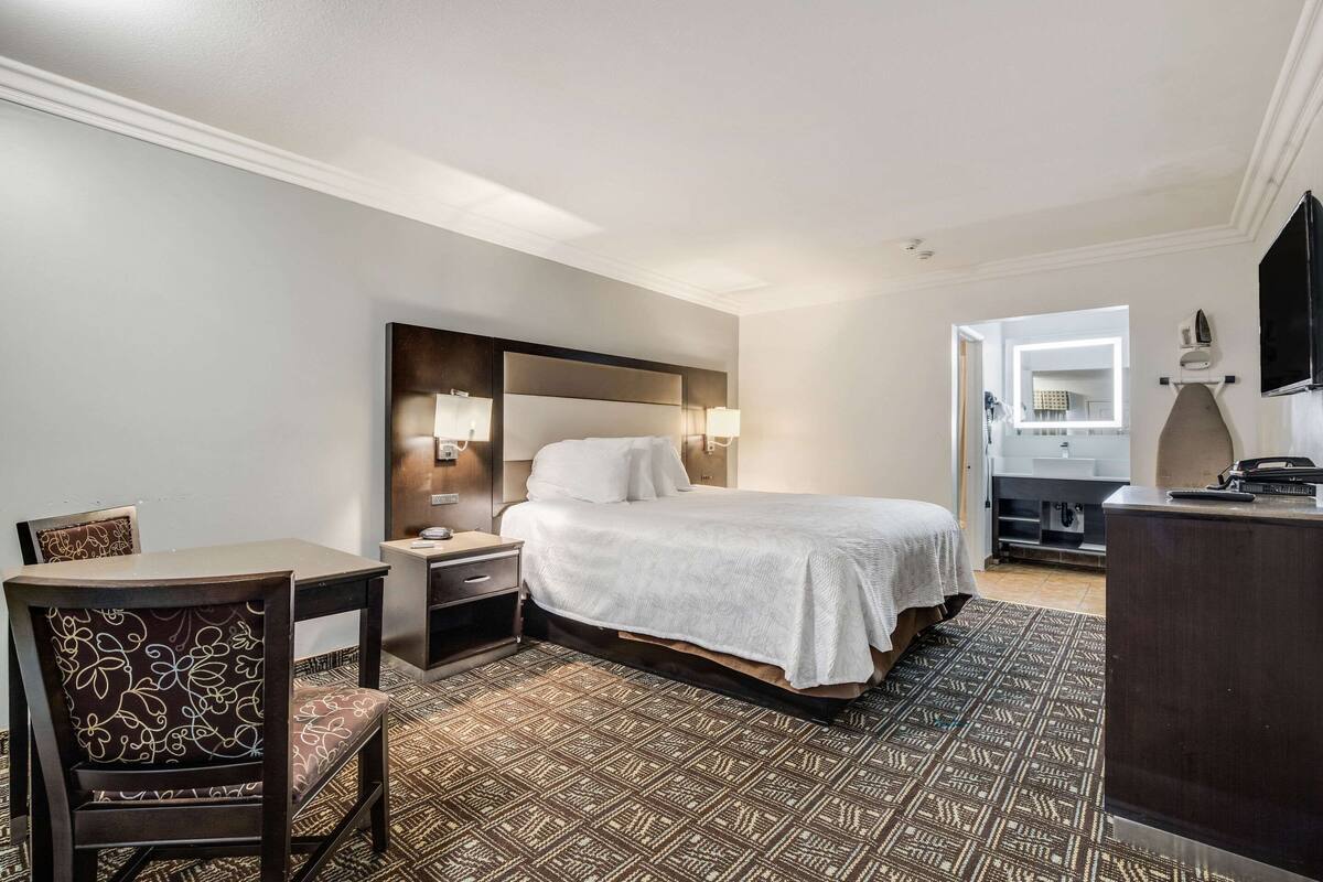 A hotel room with a bed, a desk, a chair, a dresser, and a mirror.