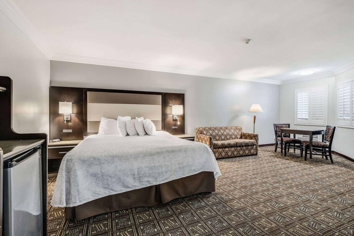 A hotel room with a large bed, a desk, a chair, and a patterned carpet.