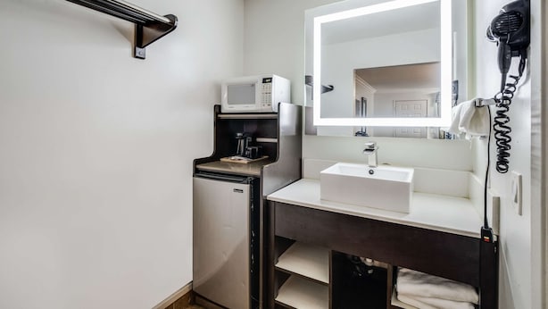A compact bathroom with a white sink, a mirror, a hairdryer, and a compact microwave. - Rodeway Inn Old Town Temecula (Temecula)