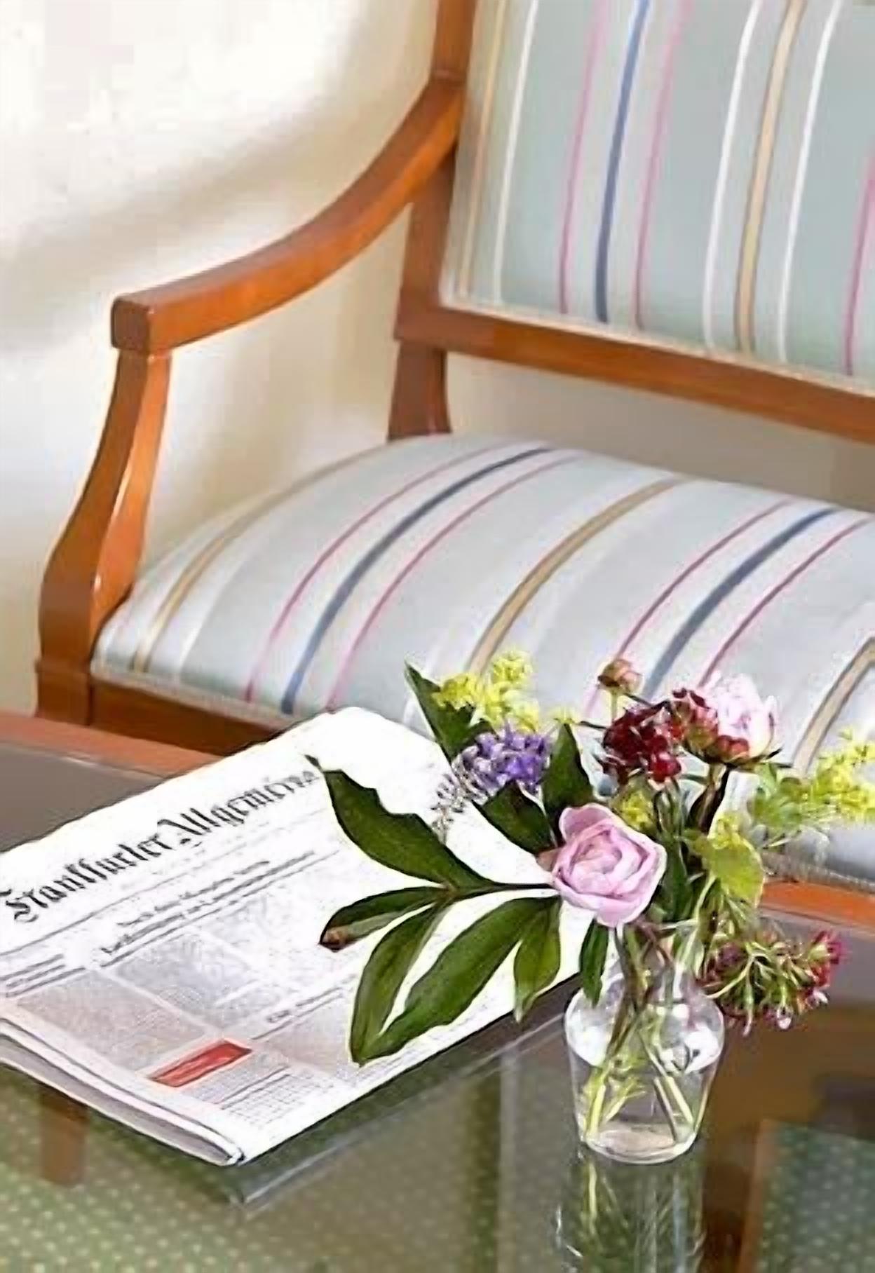A newspaper on a glass table with a vase of flowers.