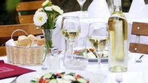 Une table dressée pour un repas, avec une bouteille de vin blanc, des verres, un panier de pain et une assiette de salade.