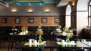Un restaurant aux murs lambrés, décoré de tableaux encadrés, et dont les tables sont ornées de sets de table jaunes et de vases remplis de fleurs.